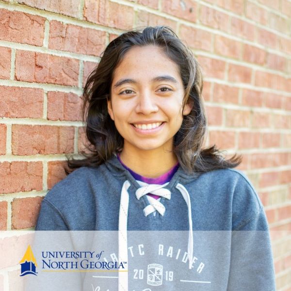 Leamsi Hernandez, a smiling student leaning against a brick wall, with the University of North Georgia logo in the bottom left corner.