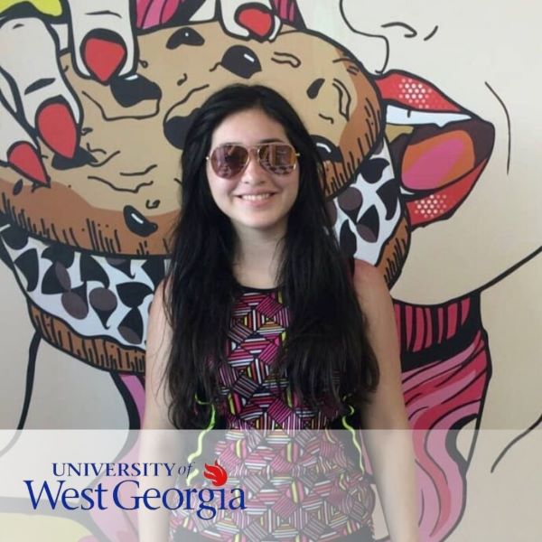 Magali Milian, smiling in front of a painting of a woman eating an ice cream sandwich.