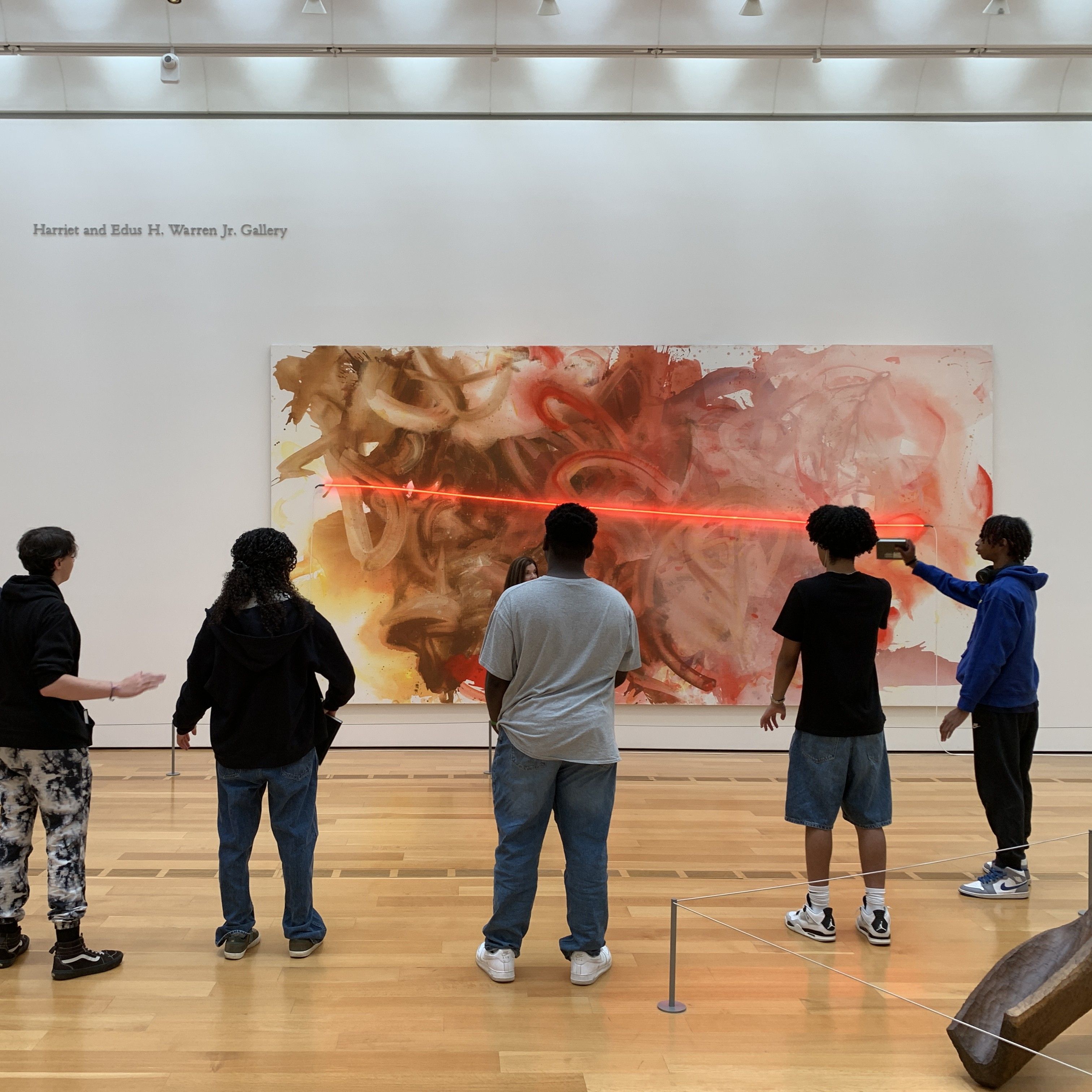 Students take in a piece of modern art with a flash of neon red streaking across the canvas.