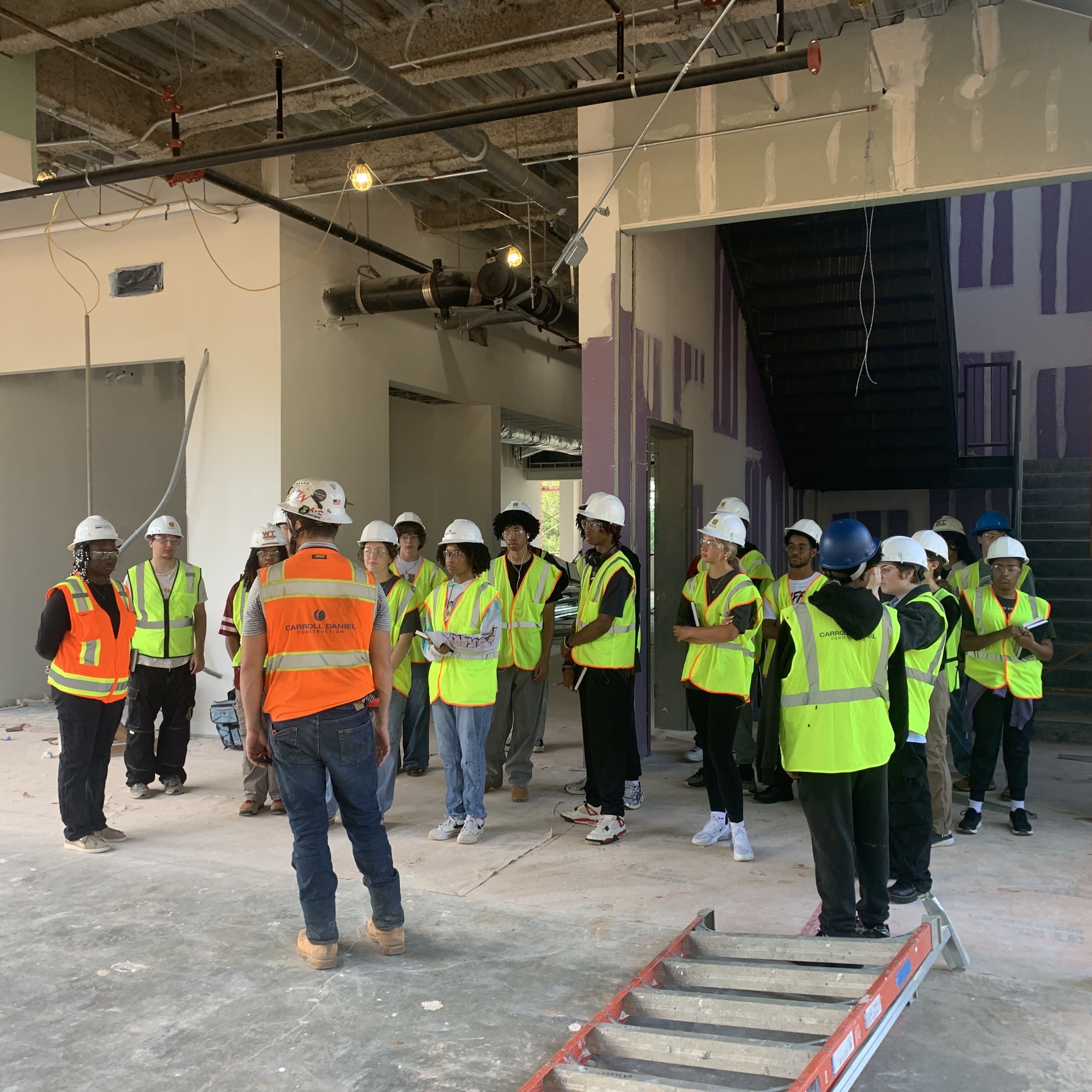 Students tour the inside of a construction site surrounded by incomplete walls. 