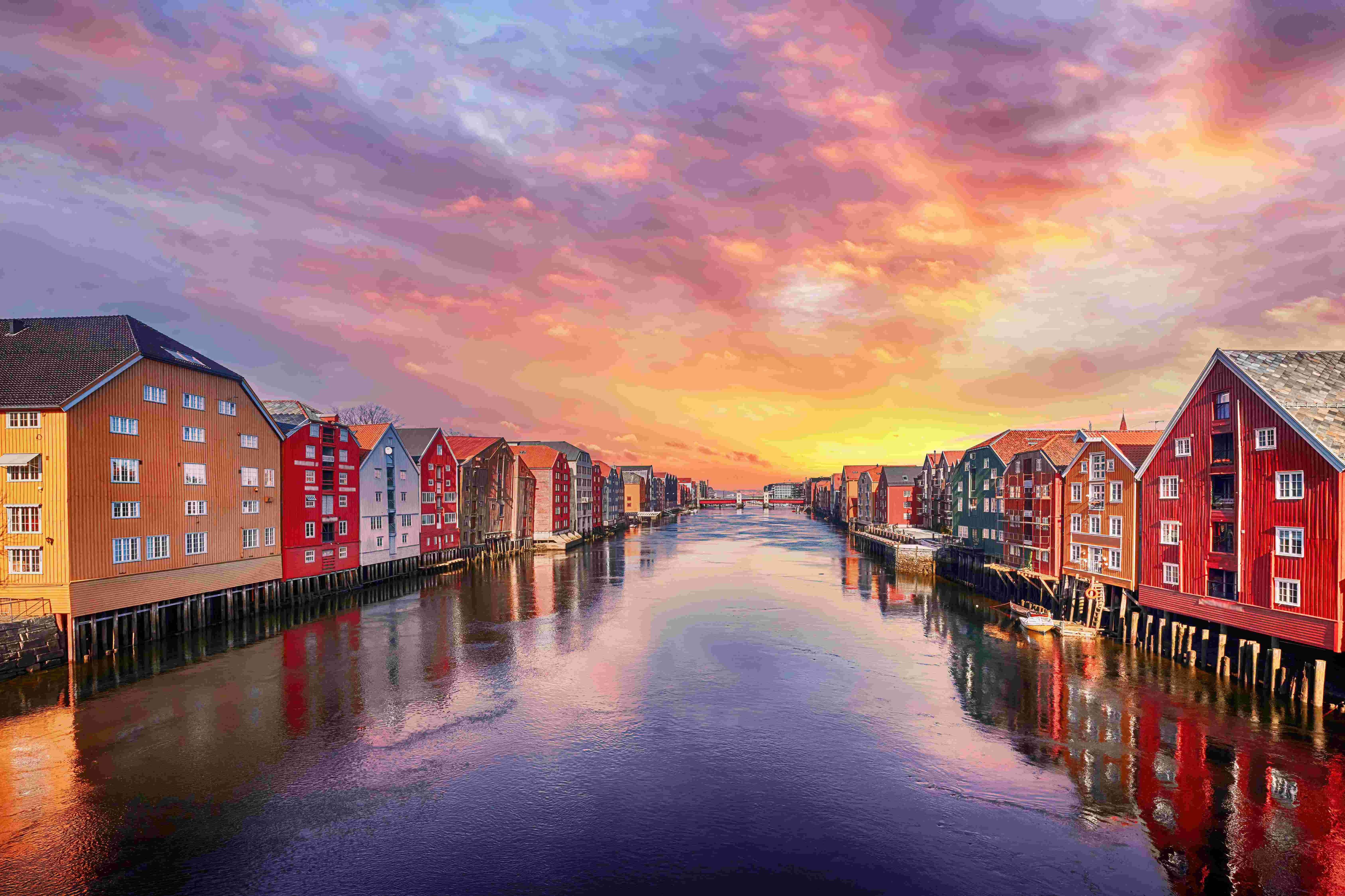 “A picturesque sunset view of the multicolored buildings lining the river in Trondheim, Norway.