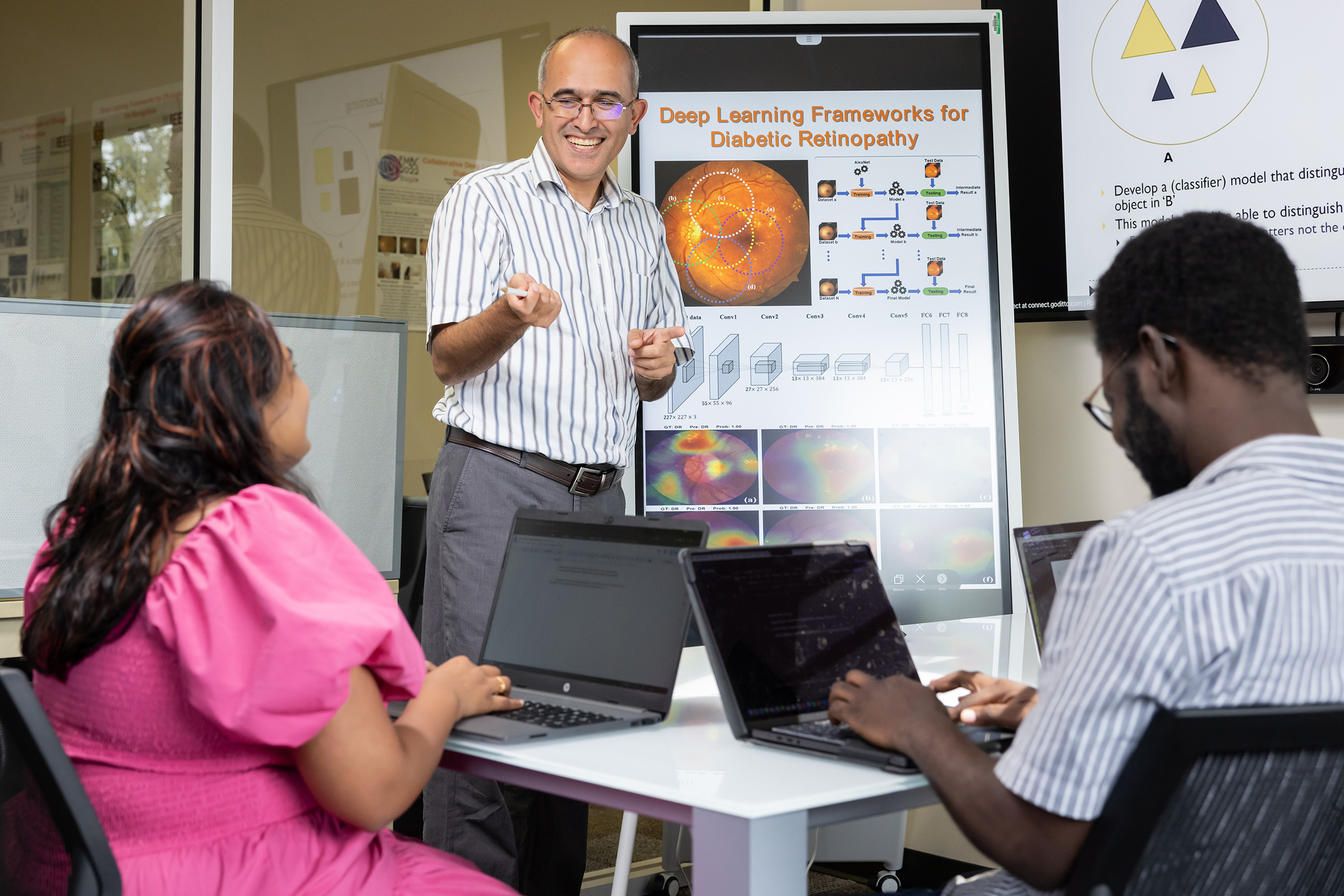 teacher standing up in class with two students at desk