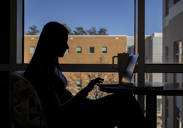 a student is studying on her latop in front of a window