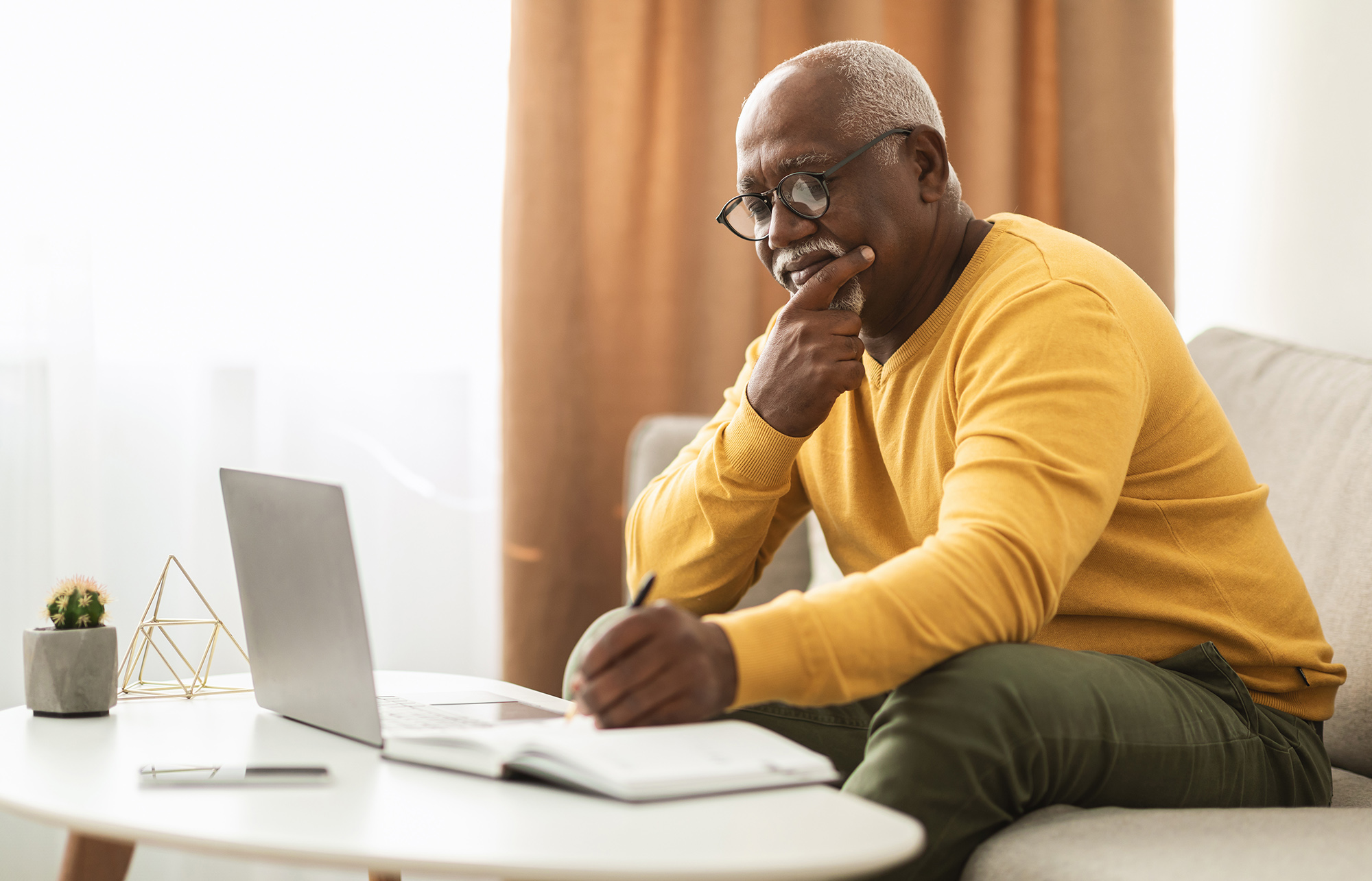 a man write in a journal with a laptop
