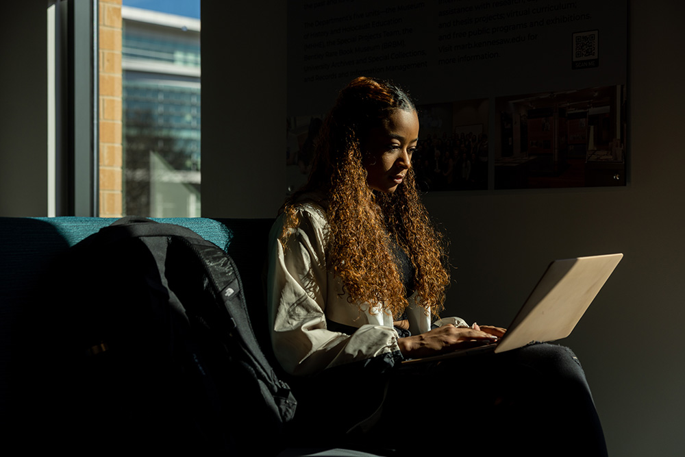 A KSU student sits with a laptop in a dark room.