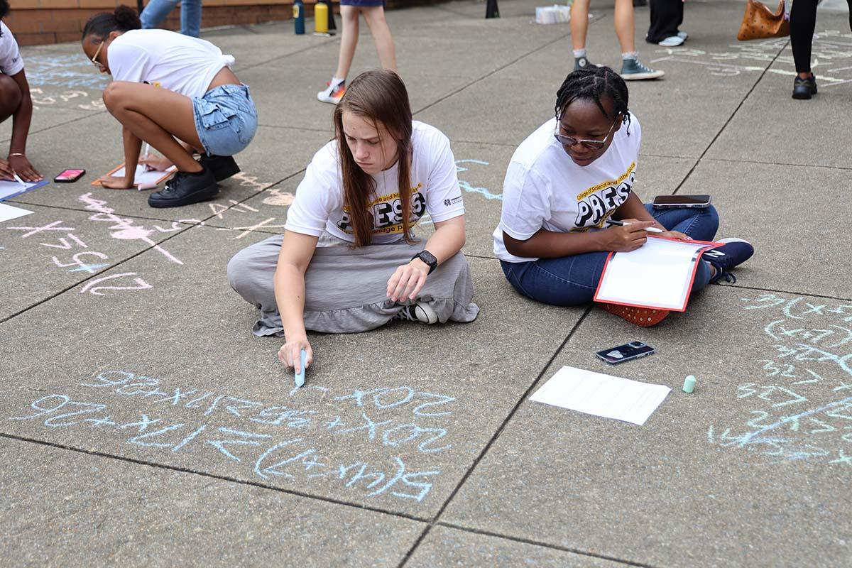 PRESS students from the college of science and mathematics sit on the pavement, writing math equations with chalk as part of an engaging group activity.  / PRESS students from the college of science and mathematics sit on the pavement, writing math equations with chalk as part of an engaging group activity. 