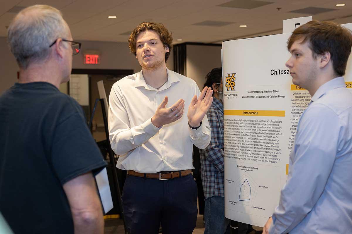 Photo of a student giving a research poster presentation. / Photo of a student giving a research poster presentation.