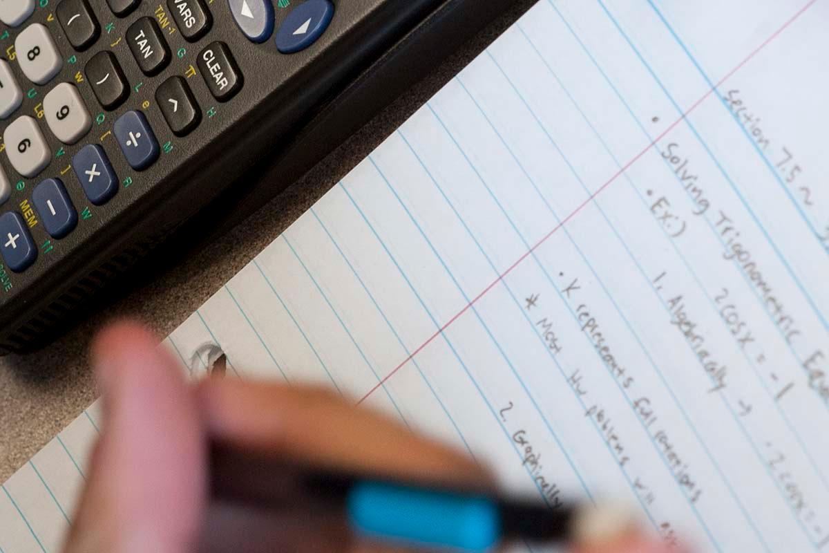 Student writing mathematics equations on paper using a calculator.   / Student writing mathematics equations on paper using a calculator.  