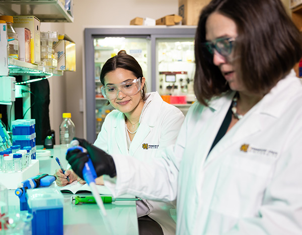 Two researchers in a biomedical lab at Kennesaw State University conducting experiments with pipettes and equipment.