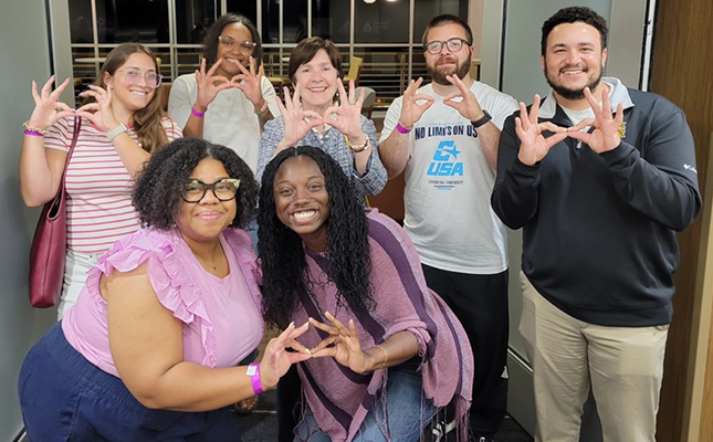 group shot of students and staff with dean in hallway showing owl signs