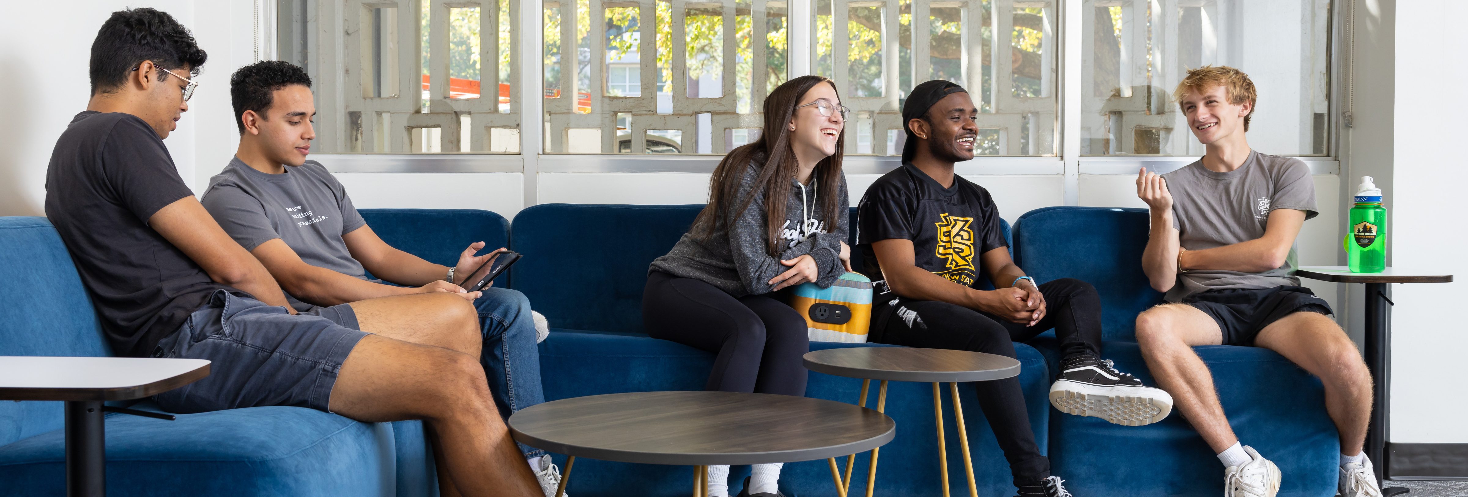 Five Kennesaw State University Honors College students mingle while sitting on a blue couch in the Marietta Honors Lounge.