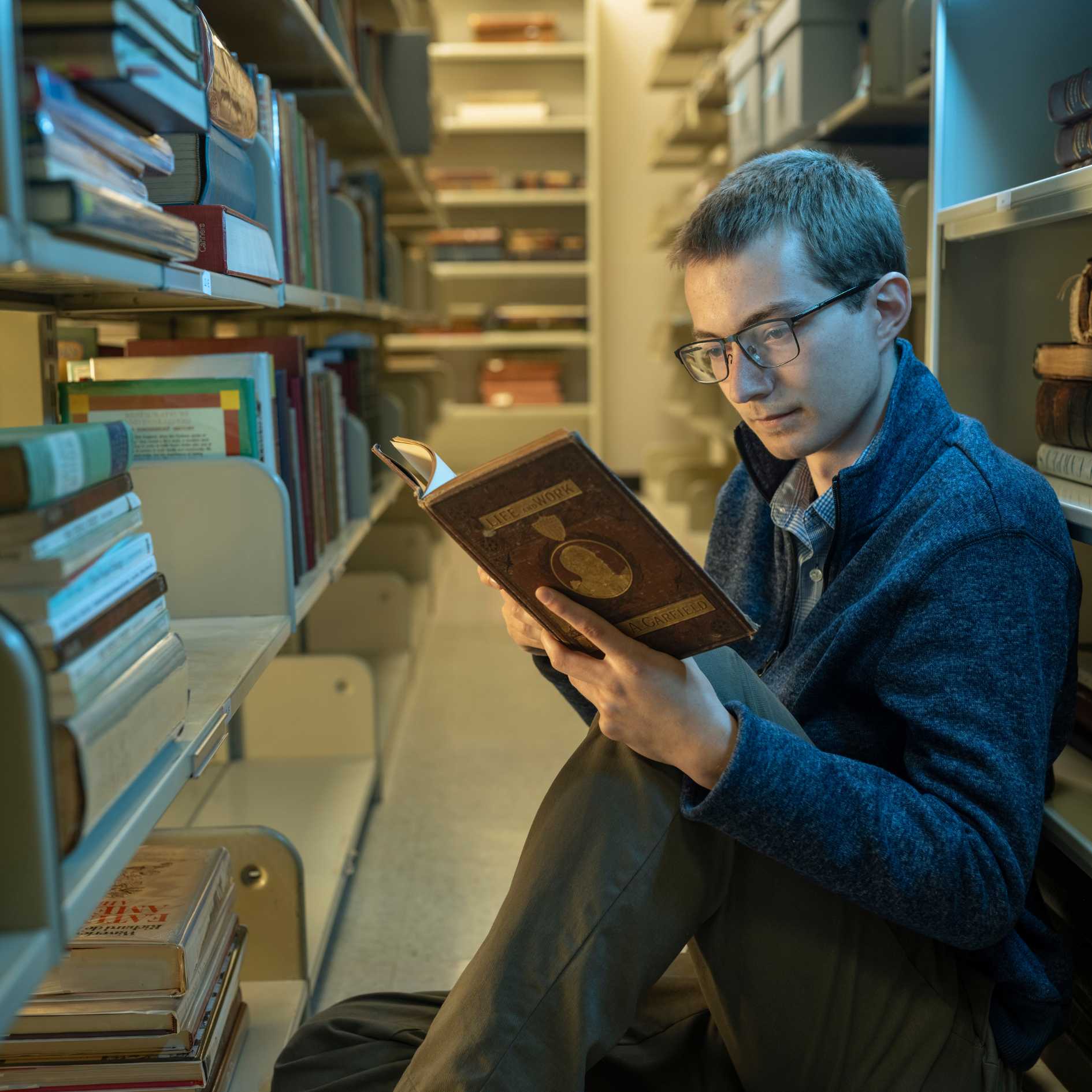 Young male student sits on the floor in the KSU Sturgis library while reading a book.