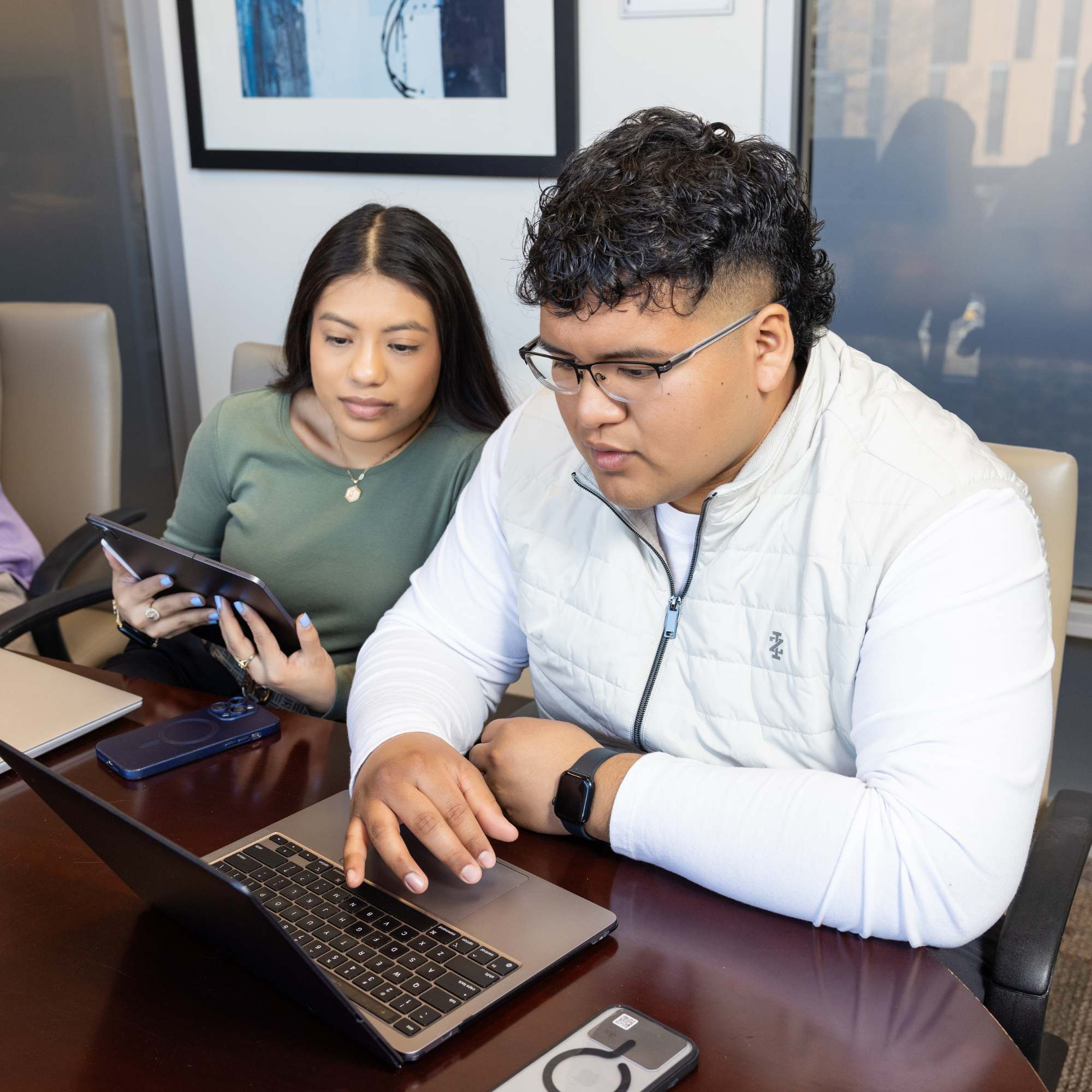 Two students collaborate using a laptop and tablet during a meeting.