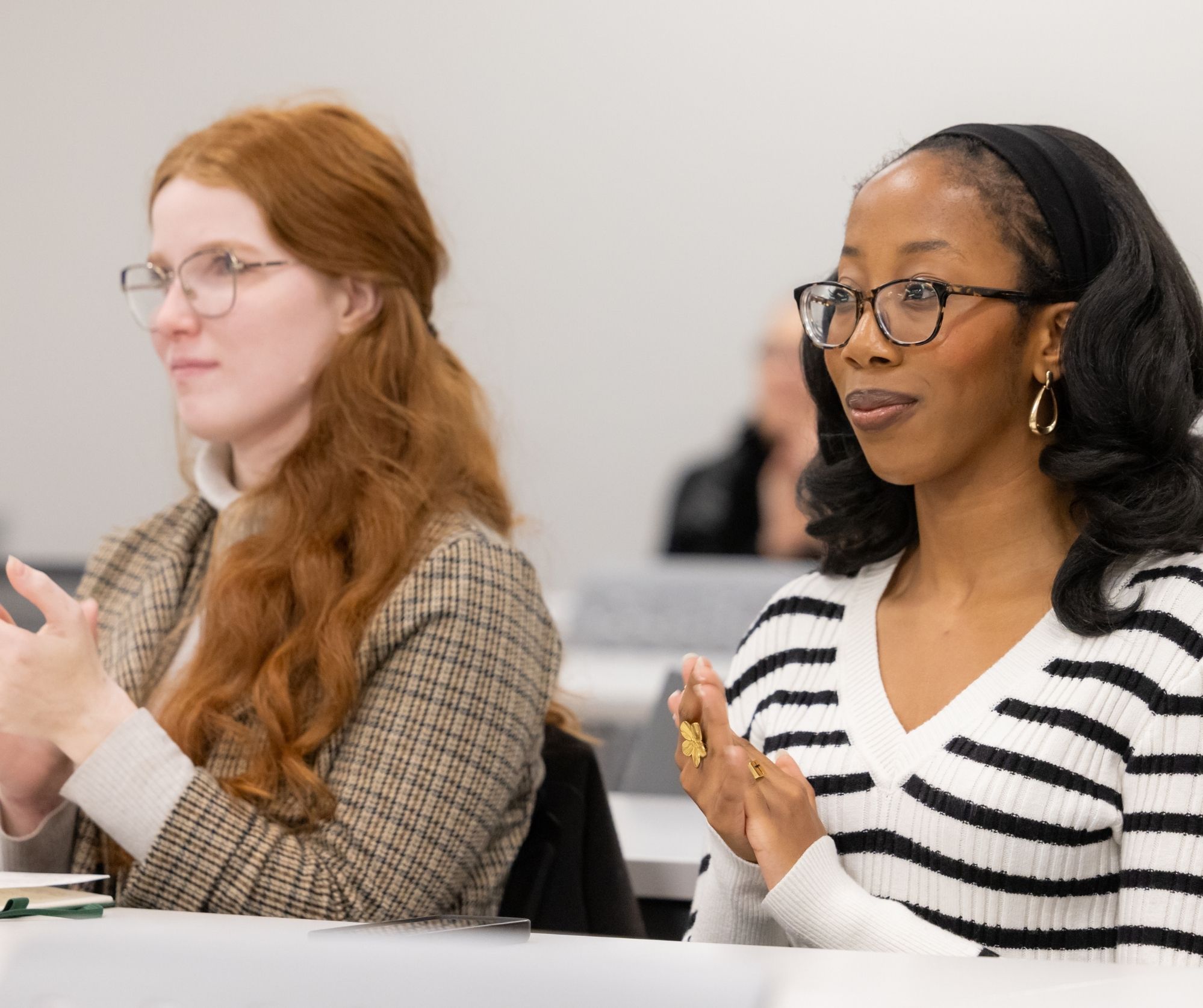 Two female students smile and clap while listening to a lecture.
