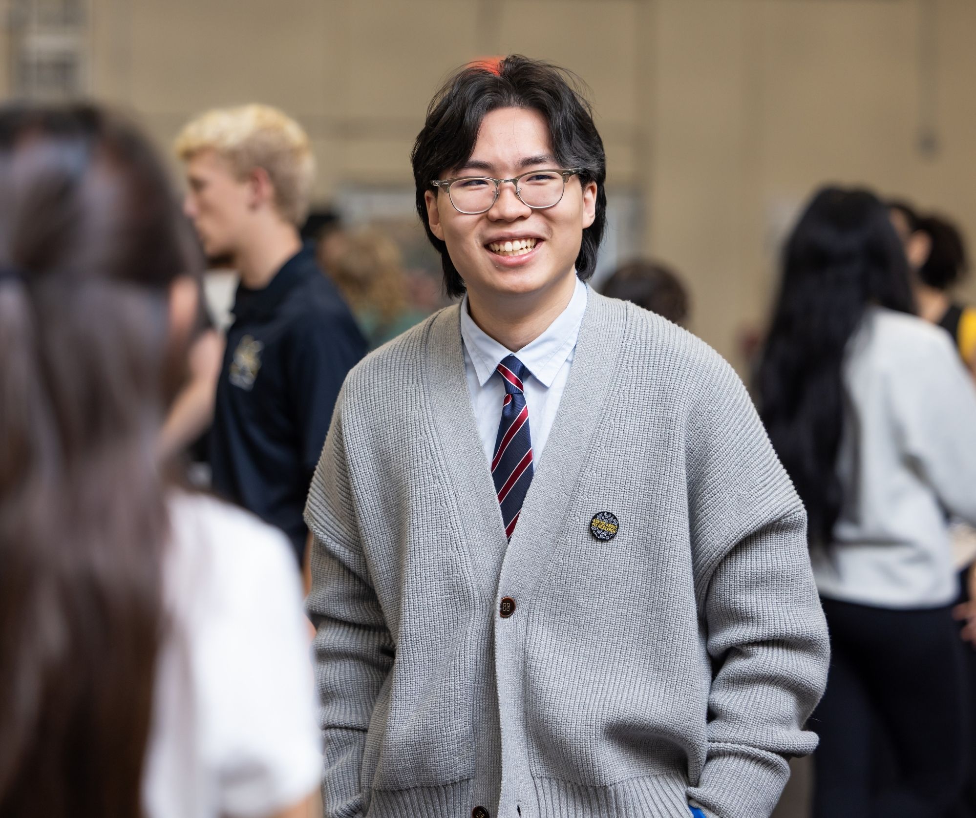 Student smiles while wearing a sweater and blue and red striped tie.