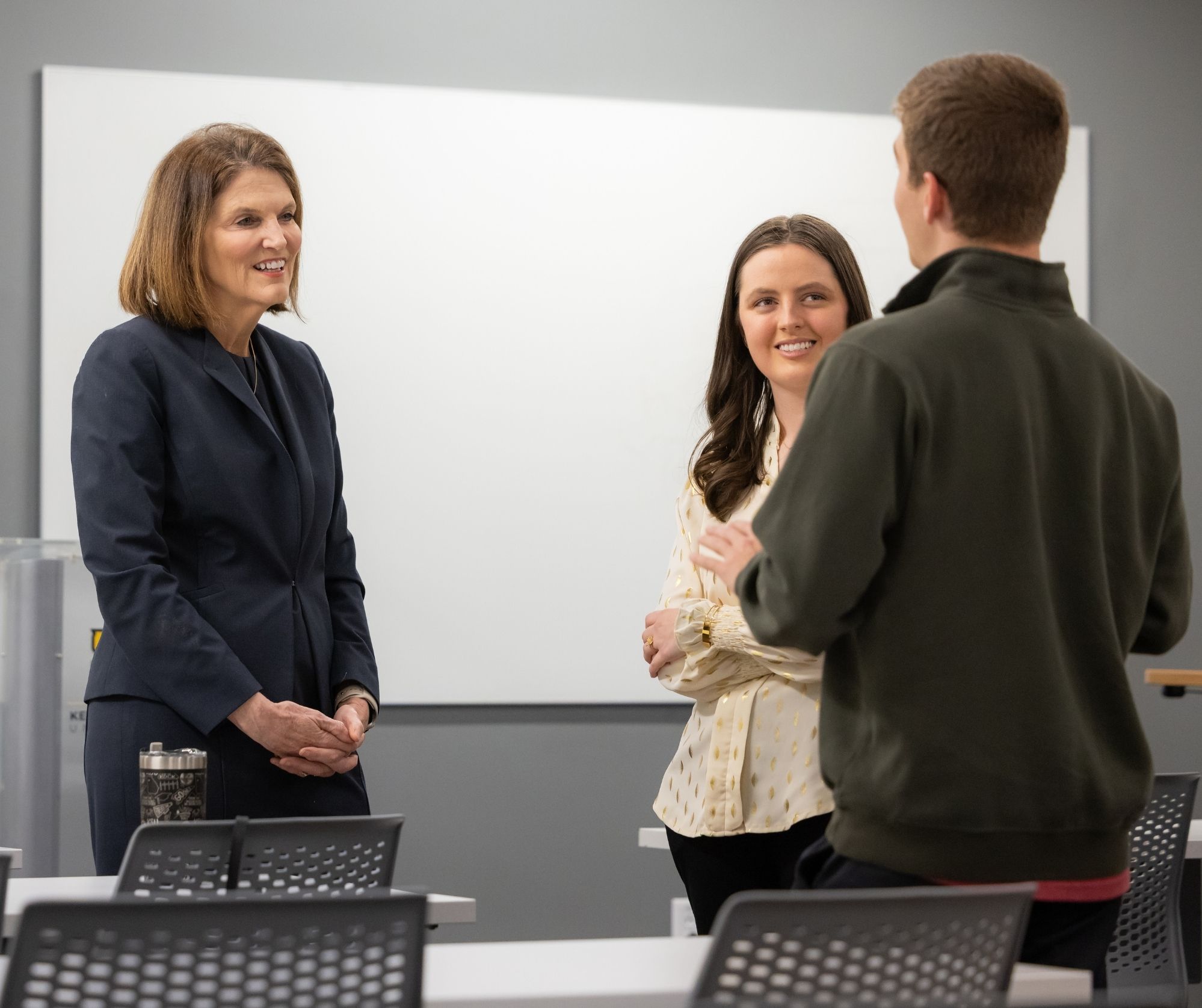 President Schwaig speaks to two students in a classroom setting.