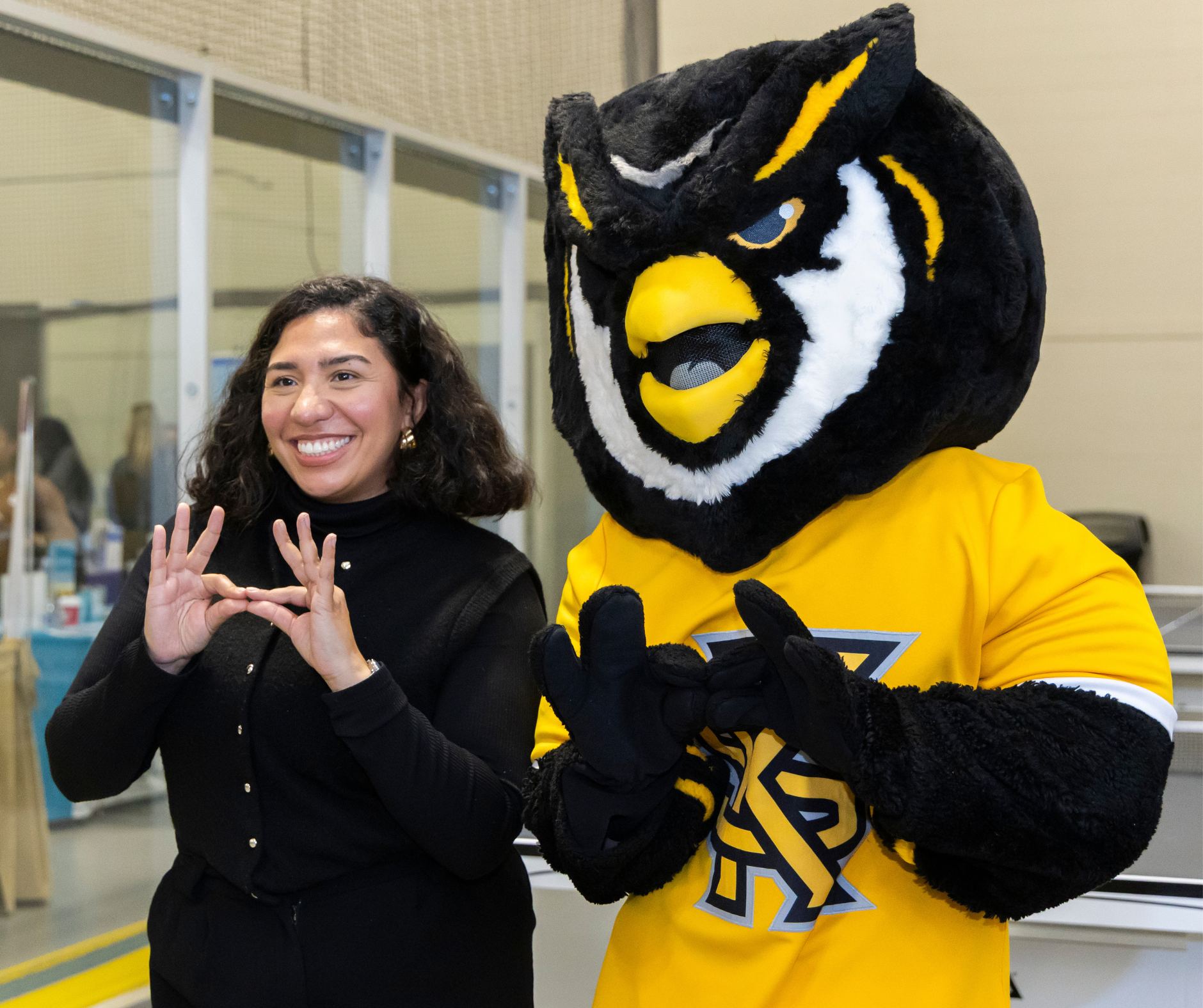 Female student and scrappy pose while holding the owl eyes hand sign.