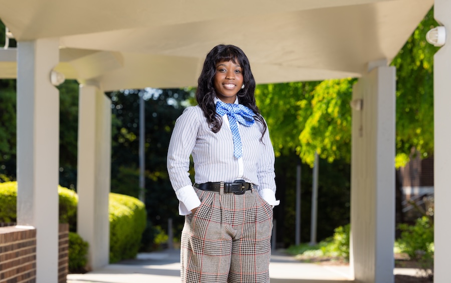 Student with hands in pocket smiling outside