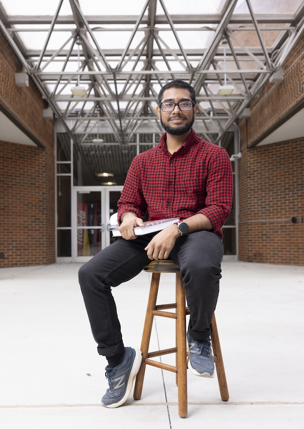 Student sitting on a stool with book in hand outside