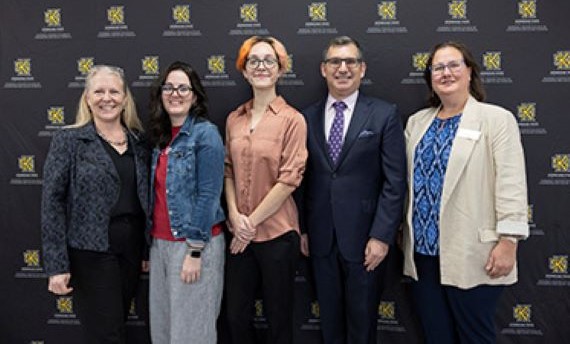 A group of five people standing in front of a black backdrop with the KSU logo on it.