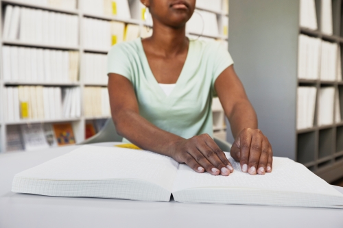 A person reads a Braille book in a library