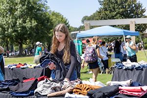 A woman holding clothes while looking through a pile of clothes at KSU's OwlSwap