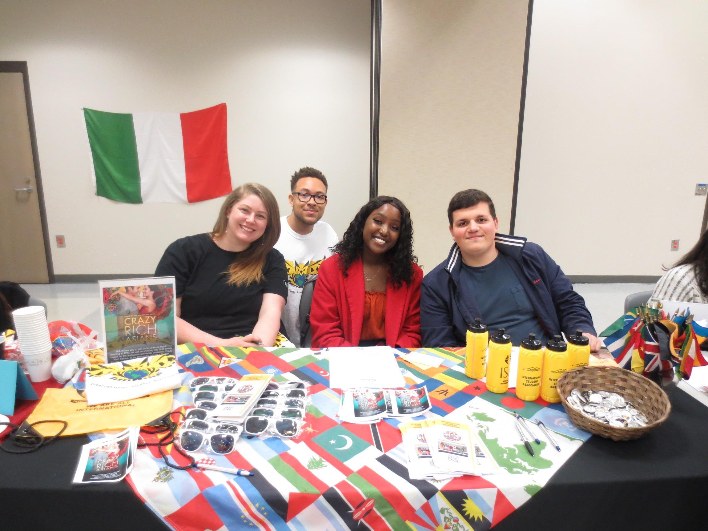  / four students at welcoming table with water bottles, pins and flags