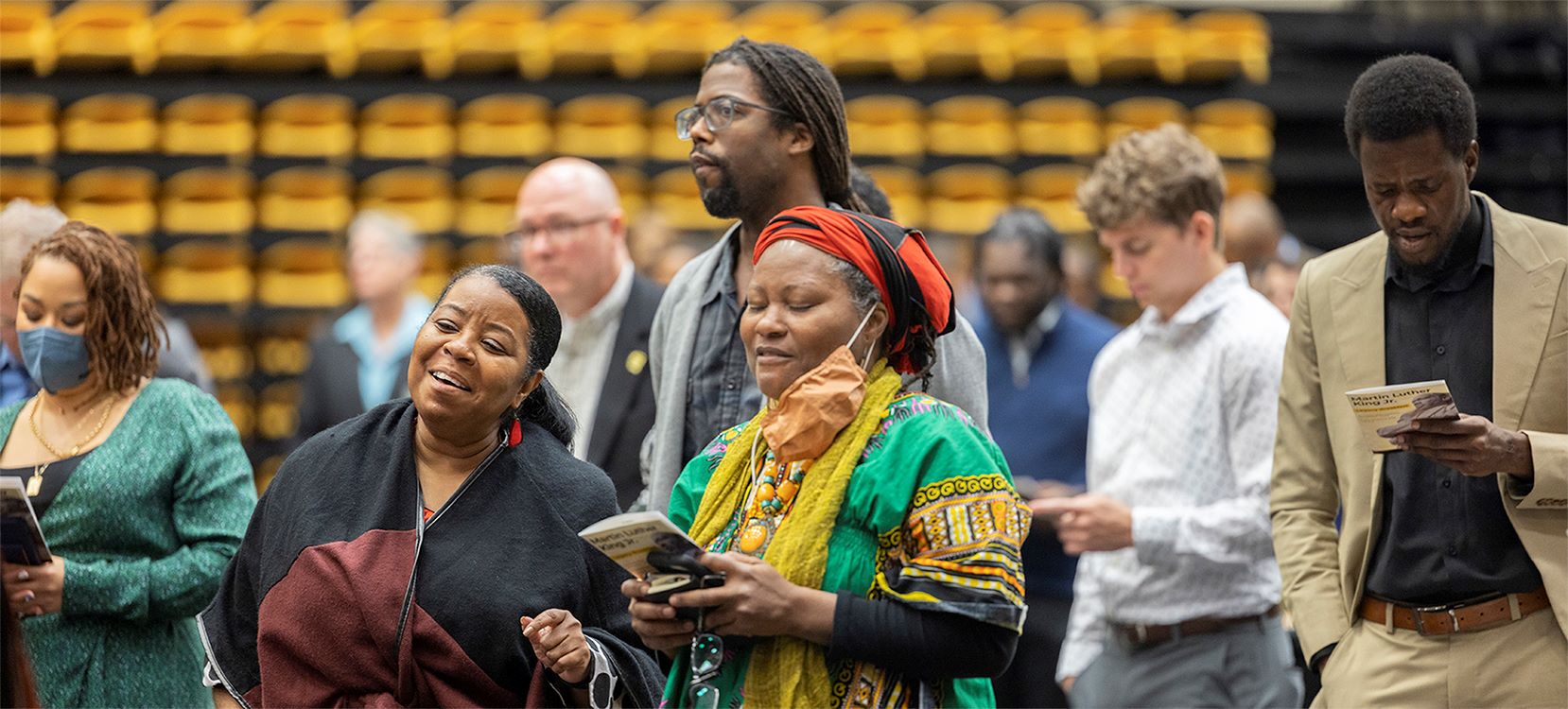 Diverse group of people attending an event, holding programs and engaging.