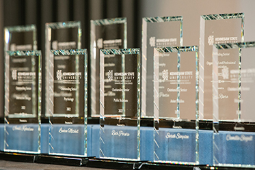 Glass awards displayed in a row, engraved with names and categories from Kennesaw State University.
