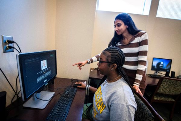 A woman using a desktop computer, while another woman points at the computer screen.