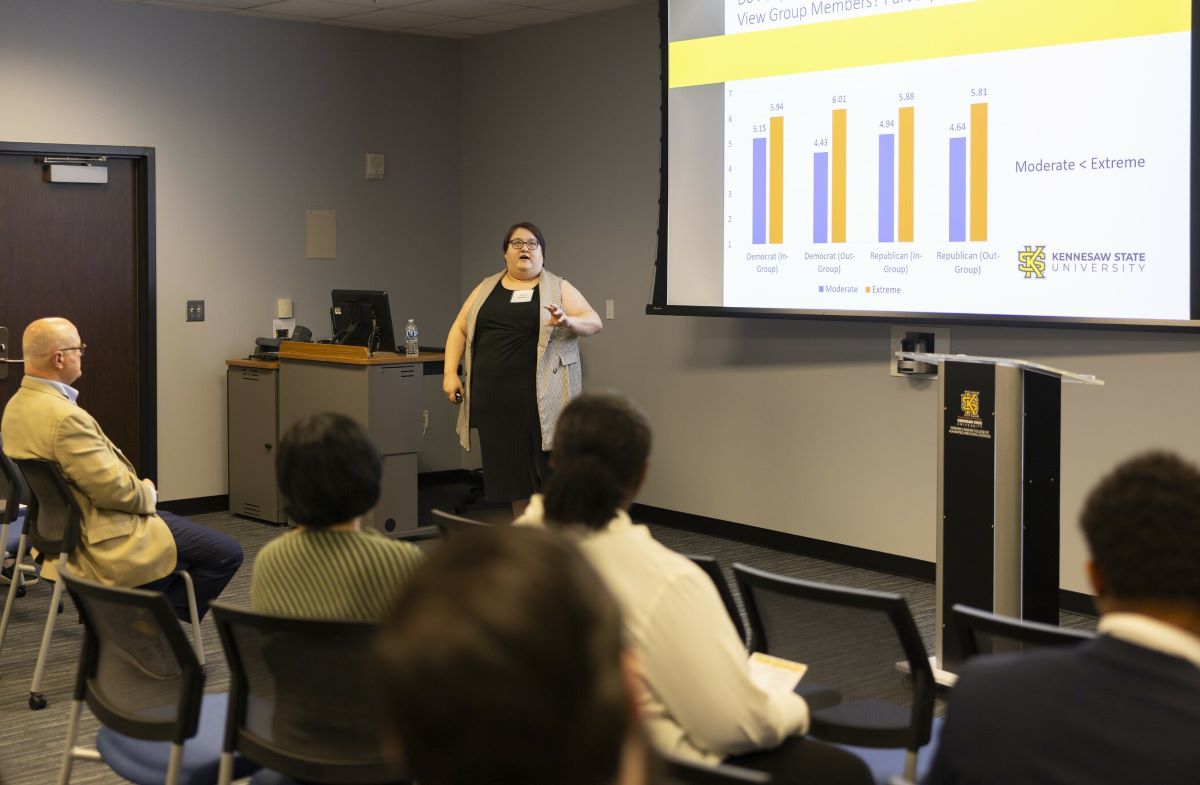 Presenter giving a lecture with a bar chart slide at Kennesaw State University while an audience listens.