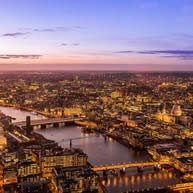 London skyline at dusk, featuring illuminated buildings and a colorful sunset sky.