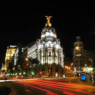 A city street at night illuminated by traffic lights, with tall buildings lining both sides of the road