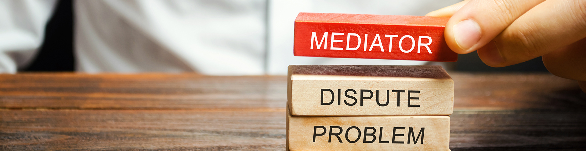 Hand placing red block the reads "Mediator" on top of wood blocks that read "Dispute" and "Problem"
