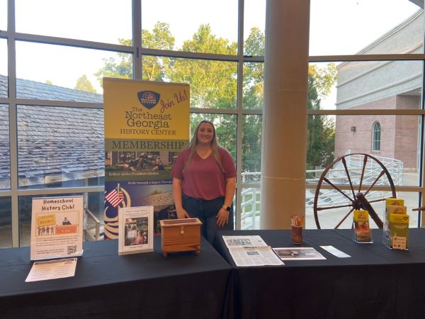 A woman standing behind a table with signs displayed for a history club and a history center membership.