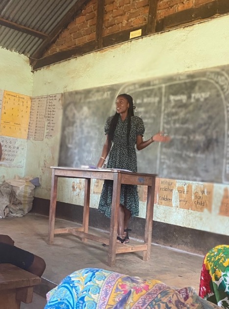 Alana Hunter, standing at a desk in a classroom setting in Africa.