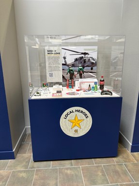 A "Local Heroes" museum display featuring military-themed items and a photo of service members near a helicopter.