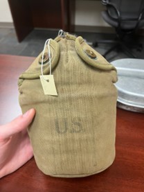 A vintage U.S. military canteen in a khaki canvas cover, held by a person.