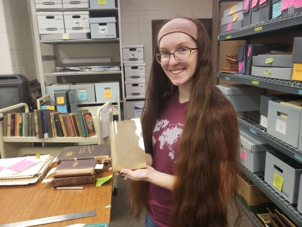 A woman smiling and holding a book at KSU's Department of Museums, Archives and Rare Books