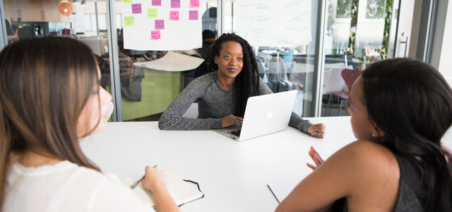 Three women having a discussion in a modern office setting.