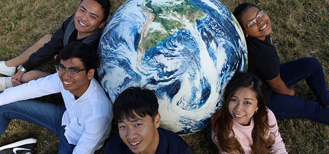 Students sitting around a large globe, smiling.