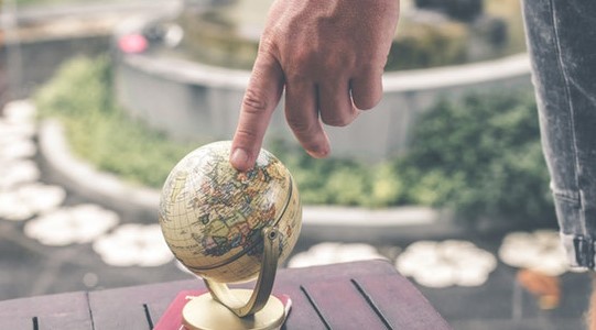 A finger pointing to a small globe on a table.