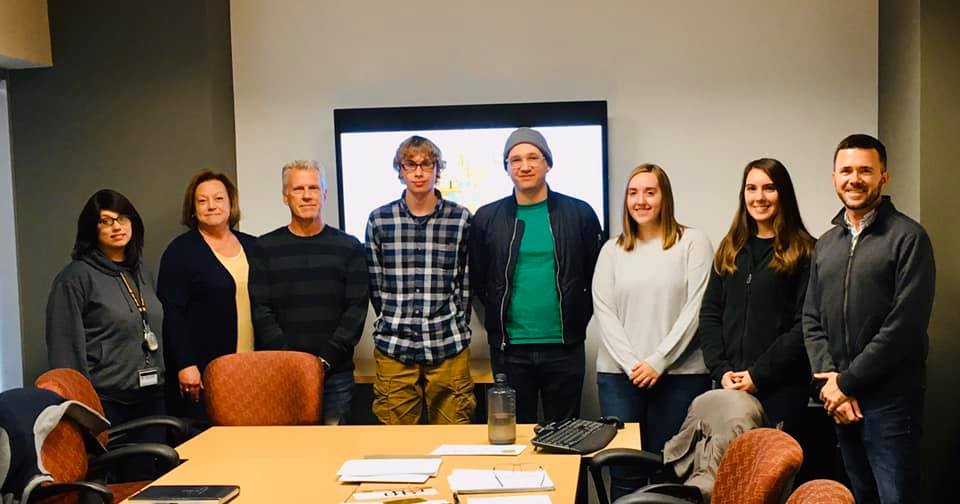Members of Gamma Theta Upsilon, standing around a table and chairs.