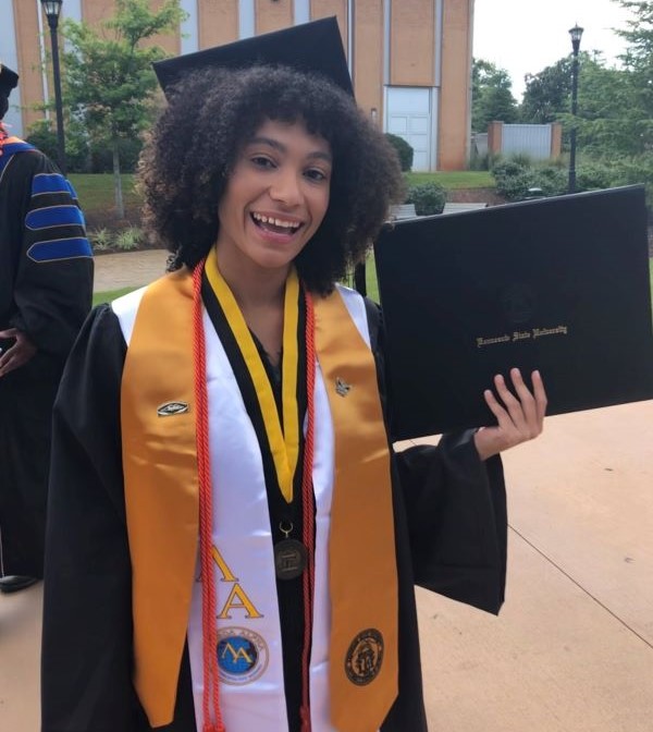 Smiling graduate in cap and gown holding diploma.