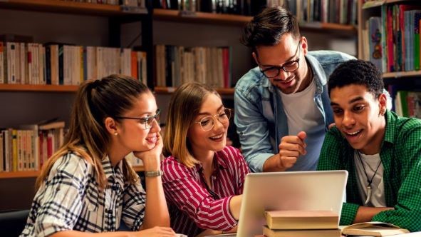 Four students in a library, looking at a tablet