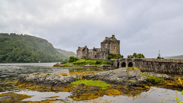 Eilean Donan Castle in Scotland, situated on a small island and connected by a stone bridge, surrounded by water and hills under a cloudy sky.