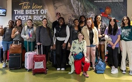 KSU students posing in front of a sign that says "Take home the best of Costa Rica."