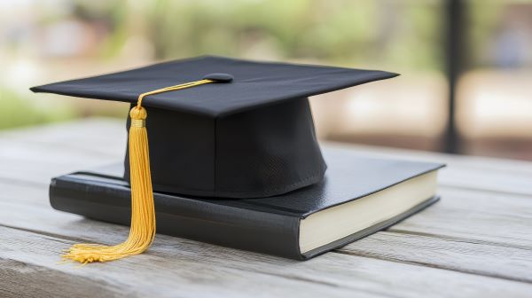 Graduation cap and book on a wooden table.