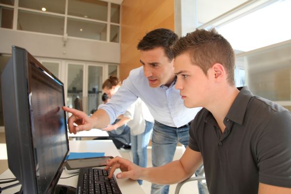 Two men using a desktop computer, in a workplace setting.
