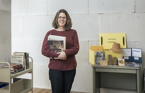 A woman smiling and holding books in a library setting.